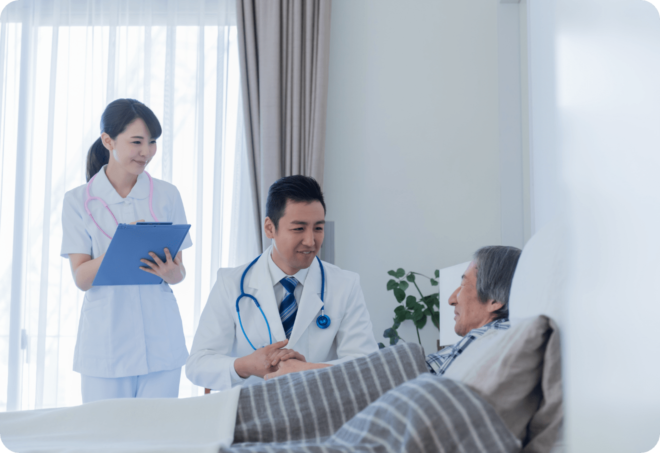 ベッドに横たわる患者の手を取りながら話をする医師と、その様子を見守る看護師。