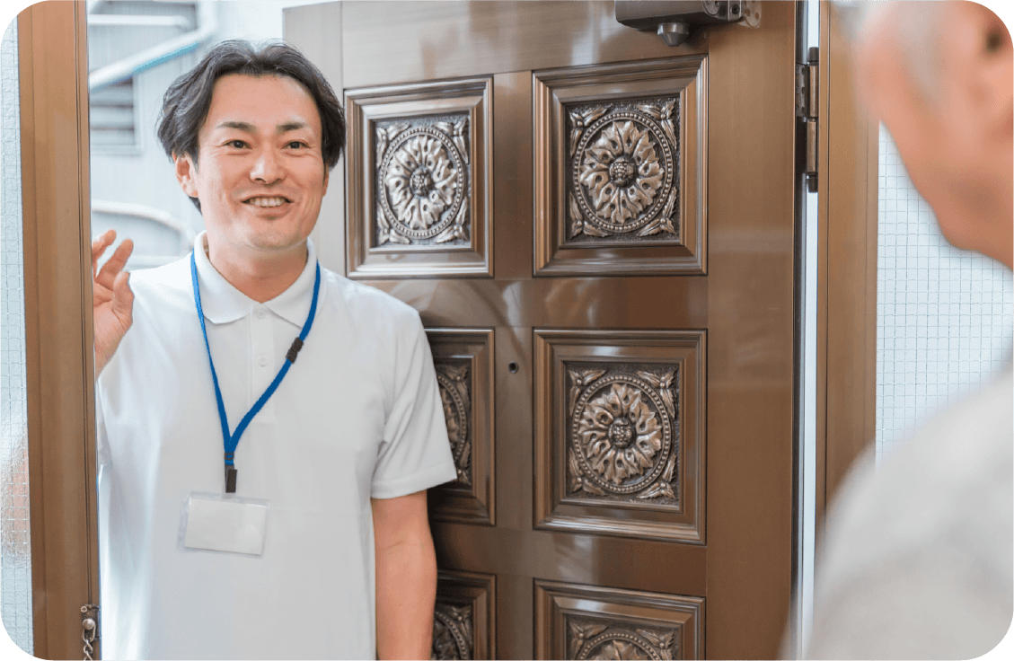 笑顔の男性ケアマネージャーが自宅訪問で利用者を出迎える様子。ケアプラン作成の打ち合わせ。