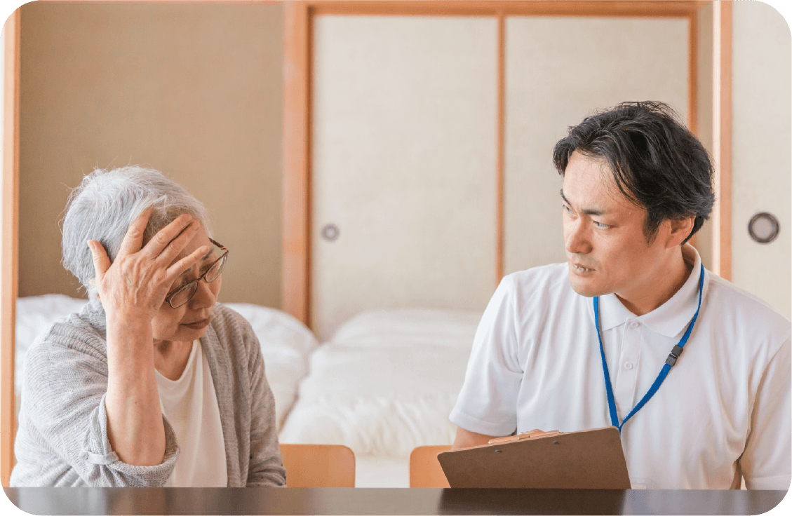 心配そうな高齢女性と話す男性ケアマネージャー。ケアプランの見直し相談。