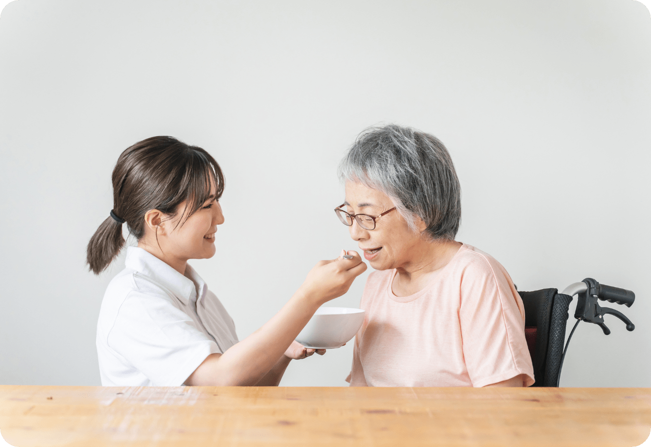 看護スタッフが高齢の女性に食事を介助しながら笑顔で向かい合っている様子